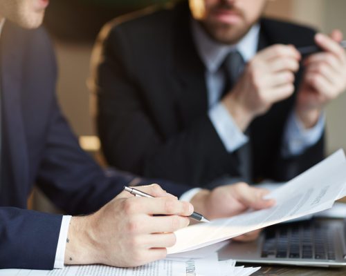 Closeup portrait of two unrecognizable  business partners reviewing paperwork and signing contract papers at table during meeting